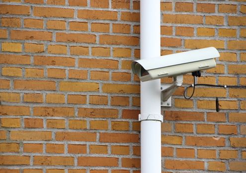Surveillance Camera with Wire mounted on Yellow Brick Wall