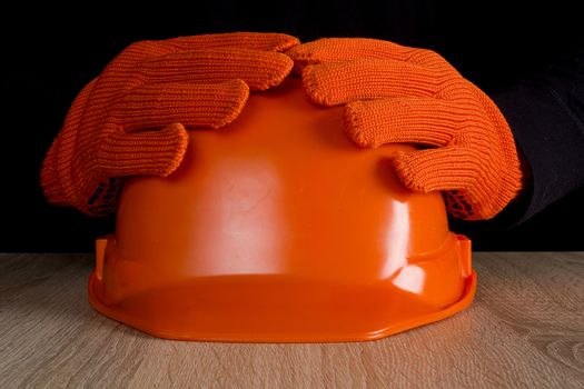 Orange construction helmet in hands on a black background