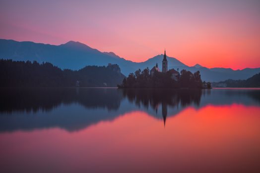 Little Island with Catholic Church in Bled Lake, Slovenia at Beautiful Red Sunrise with Castle and Mountains in Background