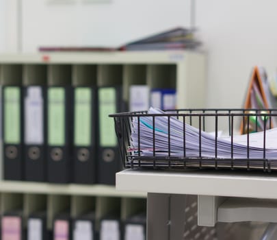 Stack of documents  in black basket on table at office.