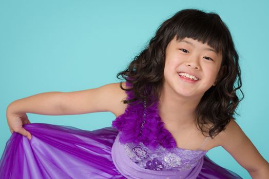 A portrait of a cute, happy and young Japanese girl in a purple dress on a blue background.