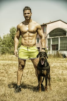 Full Body Shot of a Shirtless Athletic Young Man with his Dog and Looking at Camera
