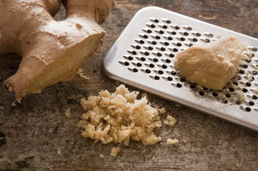 One stainless steel grater next to whole ginger root and shreds on a rustic table