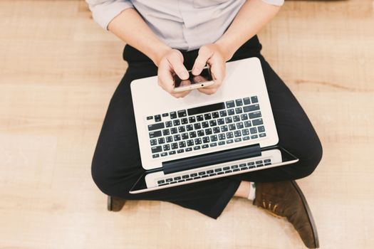 Top view man typing text message on his smart phone while sitting front open laptop computer, office man connecting to wireless via notebook and mobile phone while he keyboarding .