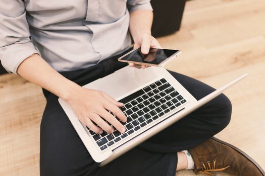 Top view man typing text message on his smart phone while sitting front open laptop computer, office man connecting to wireless via notebook and mobile phone while he keyboarding .