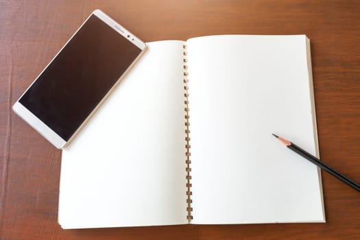 Blank note book with pencil and smartphone on wooden table background concept and Idea for write your text here.