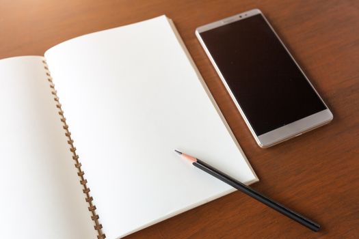 Blank note book with pencil and smartphone on wooden table background concept and Idea for write your text here.