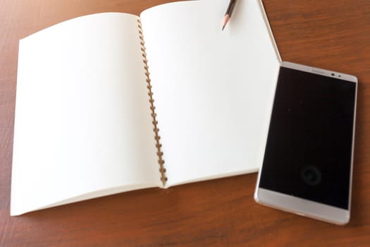 Blank note book with pencil and smartphone on wooden table background concept and Idea for write your text here.