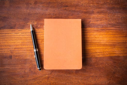 Notebook and pen on haed wood table .