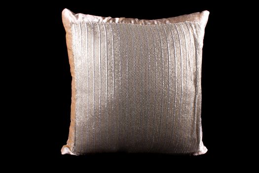 A golden and silver colored shiny pillow with sequins on black studio background.