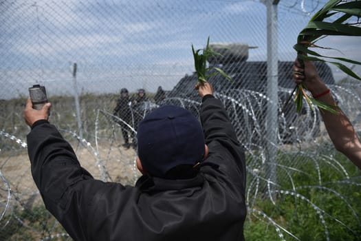 GREECE, Idomeni: A refugee holds up a used tear gas canister and leaves to Macedonian authorities near the Macedonia-Greek border on April 11, 2016 a day after clashes between the two groups.Hundreds of migrants were injured on Sunday as they attempted to cross the border into Macedonia. Police used tear gas, water cannons, and stun grenades to disperse the crowd as migrants threw stones in retaliation. 