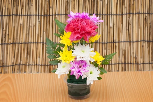 Colorful flower bouquet arrangement in vase on wood background