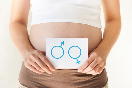 Pregnant woman holding her hands on the belly and holding a paper with symbols are boy and girl