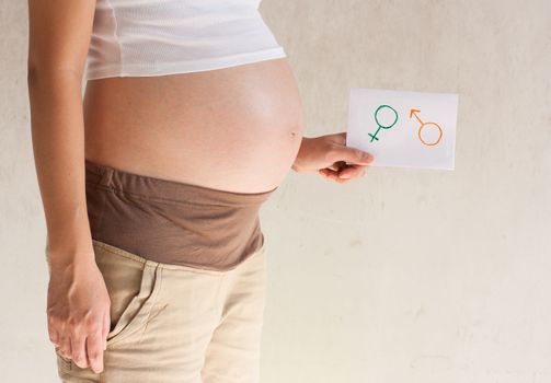 Pregnant woman holding her hands on the belly and holding a paper with symbols are boy and girl