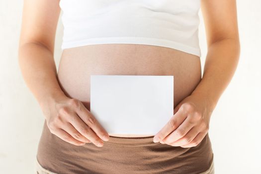 Pregnant woman holding her hands on the belly and holding a blank paper.