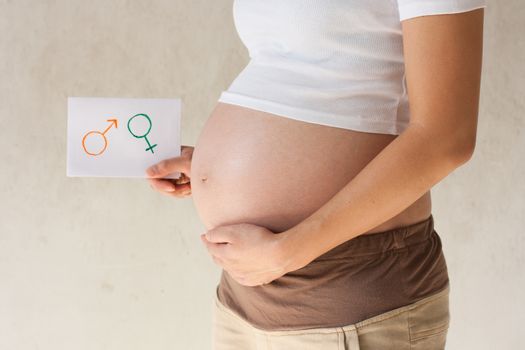 Pregnant woman holding her hands on the belly and holding a paper with symbols are boy and girl