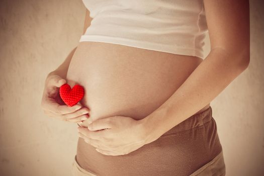 Pregnant woman holding her hand on belly And holding a red heart, Vintage filter