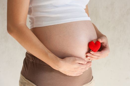 Pregnant woman holding her hand on belly And holding a red heart