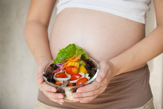 Pregnant woman's belly and vegetable salad. Healthy nutrition.