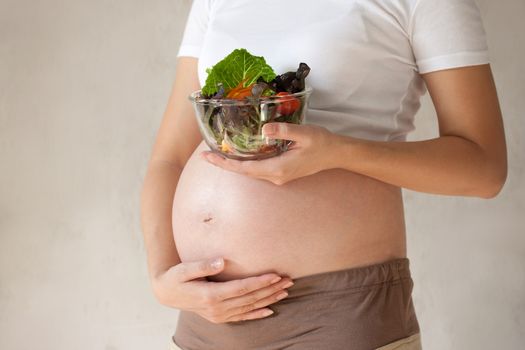 Pregnant woman's belly and vegetable salad. Healthy nutrition.