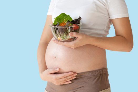 Pregnant woman's belly and vegetable salad. Healthy nutrition. isolated on blue background