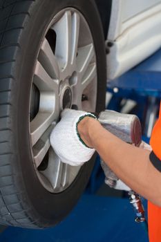 car mechanic screwing or unscrewing car wheel of lifted automobile by pneumatic wrench at repair service station