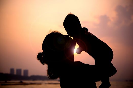 Silhouette of mother  with her toddler against the sunset and lens flare