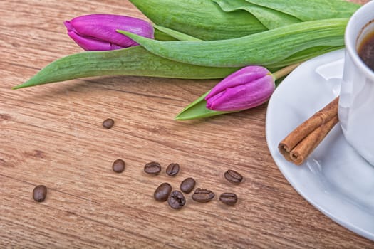 A cup of coffee with cinnamon and purple tulips on a wooden background