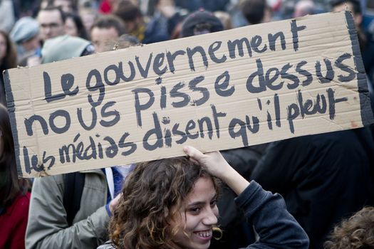 FRANCE, Paris: A woman holds a sign which reads The government piss on ourselves, mass media say it's raining as hundreds of protesters gather on the Place de La Republique in Paris as part of demonstrations by the Nuit Debout (Up All Night) movement, on April 11, 2016. French Prime Minister Manuel Valls unveiled measures to help young people find work, aiming to quell weeks of protests against the government's proposed reforms to labour laws. Young people have been at the forefront of mass demonstrations against the reforms over the past month, which the government argues are aimed at making France's rigid labour market more flexible.