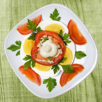 Stuffed tomatoes and eggs on the plate. Wooden background toned in green.