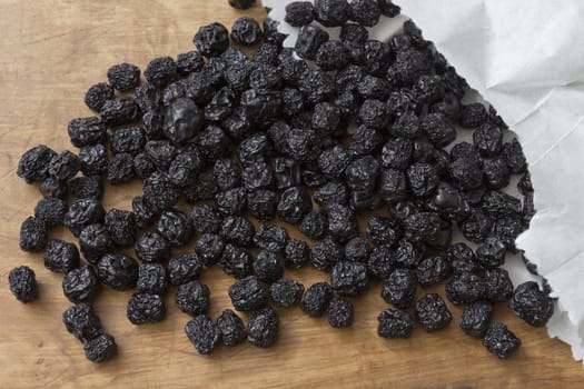 Dried aronia fruit spilled out of a paper bag on the wooden table