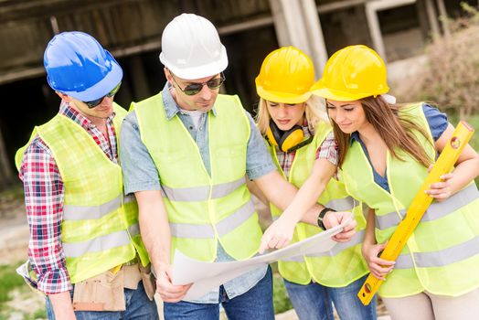 Four construction architects review plan at a construction site.