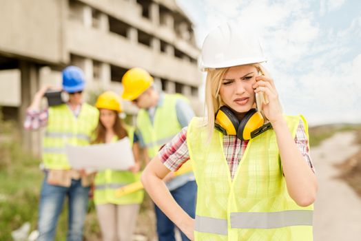 Beautiful young female construction architects using phone in front building damaged in the disaster.