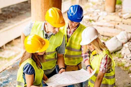 Four construction architects review plan in front building damaged in the disaster.