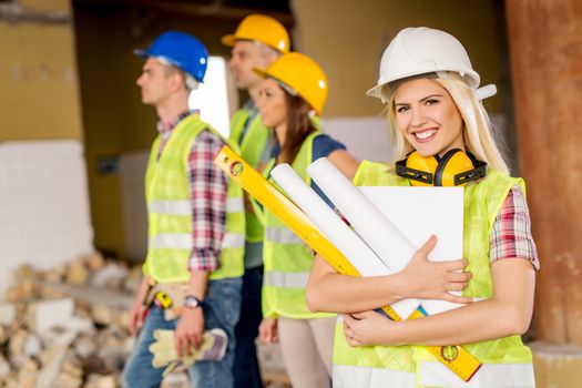 Beautiful young female construction architects at a construction site. She is holding plans and smiling looking at camera.