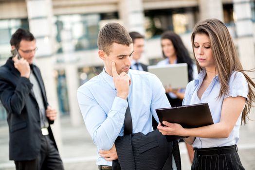 Young businessman talking to his pretty woman business partner in front of office building.