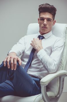 Serious well-dressed young businessman sitting looking at camera.
