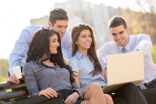 A small group of young business people sitting on a park bench and looking at the laptop.