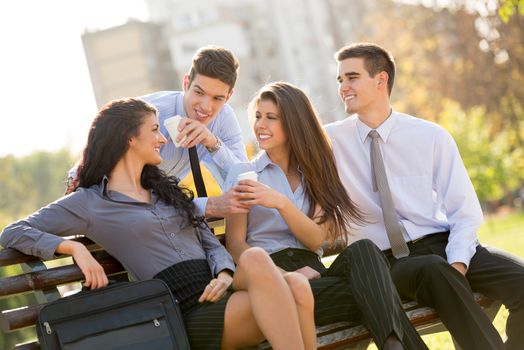 Successful young business team during a coffee break, sitting on a park bench enjoying a sunny day.