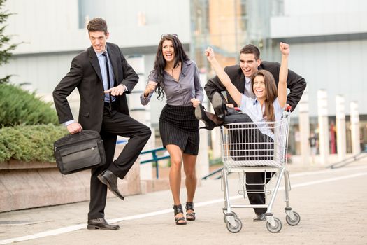 Group of young business people on the street near a supermarket in a hurry to sell, pushing his colleague in a shopping trolley.