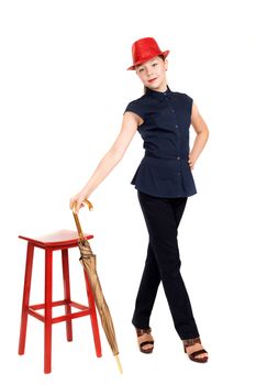 The girl the teenager in a suit and a hat with an umbrella in hands about a red chair on a white background