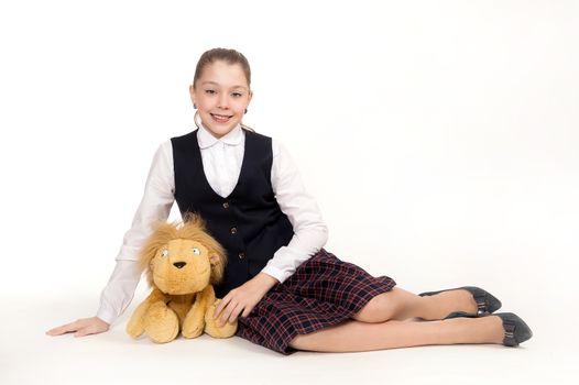 The beautiful schoolgirl sits in a school uniform and holds a toy on a white background