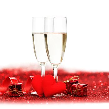 Glasses with Champagne and handmade hearts on red glitters isolated on white background