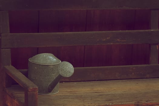 Old and rusty watering can place on wooden chair in vintage style.