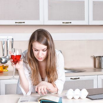 girl in a white men's shirt drinking red wine and reading a book in the kitchen. close-up