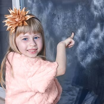 Girl 6 years old in a beautiful white dress near the winter window