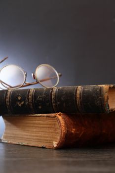 Vintage still life with spectacles on stack of old books on dark background