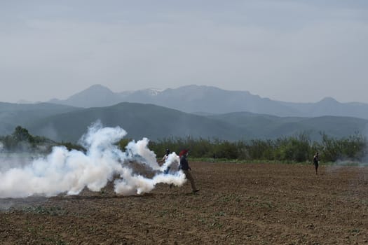 GREECE, Idomeni: Two men throw back to Macedonian police a tear gas shell as migrants and refugees tried to break down the border fence near their makeshift camp at the Greek-Macedonian border near Idomeni village, on April 13, 2016. About 100 migrants spread out over about 100 metres (yards) tugging at the wire fence, but swiftly pulled back when two squads of Greek riot police moved in, the reporter said. The Greek riot police positioned themselves between the migrants and the Macedonian fence, ending the incident.
