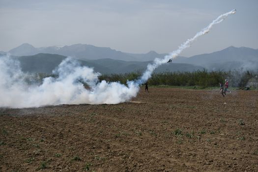 GREECE, Idomeni: A man throws back to Macedonian police a tear gas shell as migrants and refugees tried to break down the border fence near their makeshift camp at the Greek-Macedonian border near Idomeni village, on April 13, 2016. About 100 migrants spread out over about 100 metres (yards) tugging at the wire fence, but swiftly pulled back when two squads of Greek riot police moved in, the reporter said. The Greek riot police positioned themselves between the migrants and the Macedonian fence, ending the incident.