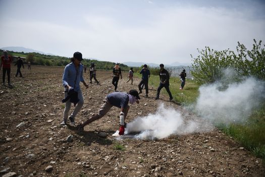 GREECE, Idomeni: A man throws back to Macedonian police a tear gas shell as migrants and refugees tried to break down the border fence near their makeshift camp at the Greek-Macedonian border near Idomeni village, on April 13, 2016. About 100 migrants spread out over about 100 metres (yards) tugging at the wire fence, but swiftly pulled back when two squads of Greek riot police moved in, the reporter said. The Greek riot police positioned themselves between the migrants and the Macedonian fence, ending the incident.